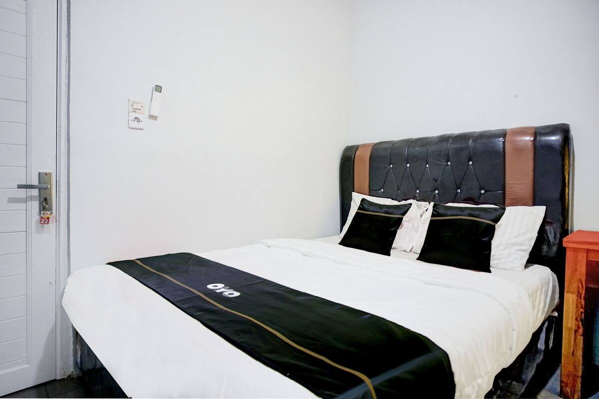A neatly made bed with a black and white duvet, a tufted headboard, and a small bedside table with a red lamp.