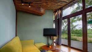 Un salon moderne avec un canapé jaune, une table ronde en bois et un téléviseur à écran plat fixé au mur.