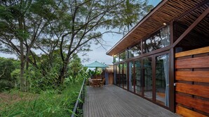 Une terrasse en bois avec des portes vitrées, entourée d’une végétation luxuriante.