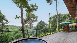 Une terrasse en bois avec un jacuzzi, le tout entouré d’une végétation luxuriante et d’arbres.