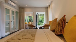 Habitación de hotel con una cama grande, vistas a zonas verdes y un área de descanso con sillas y una mesa.