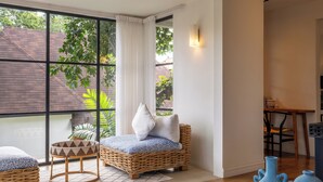 Una habitación con un ventanal grande, muebles de mimbre y una mesita.