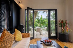 A modern living room with a sofa, patterned cushions, a dining table, and a view of a tropical garden through glass doors. - Martini Suites by Betterplace (Kerobokan)