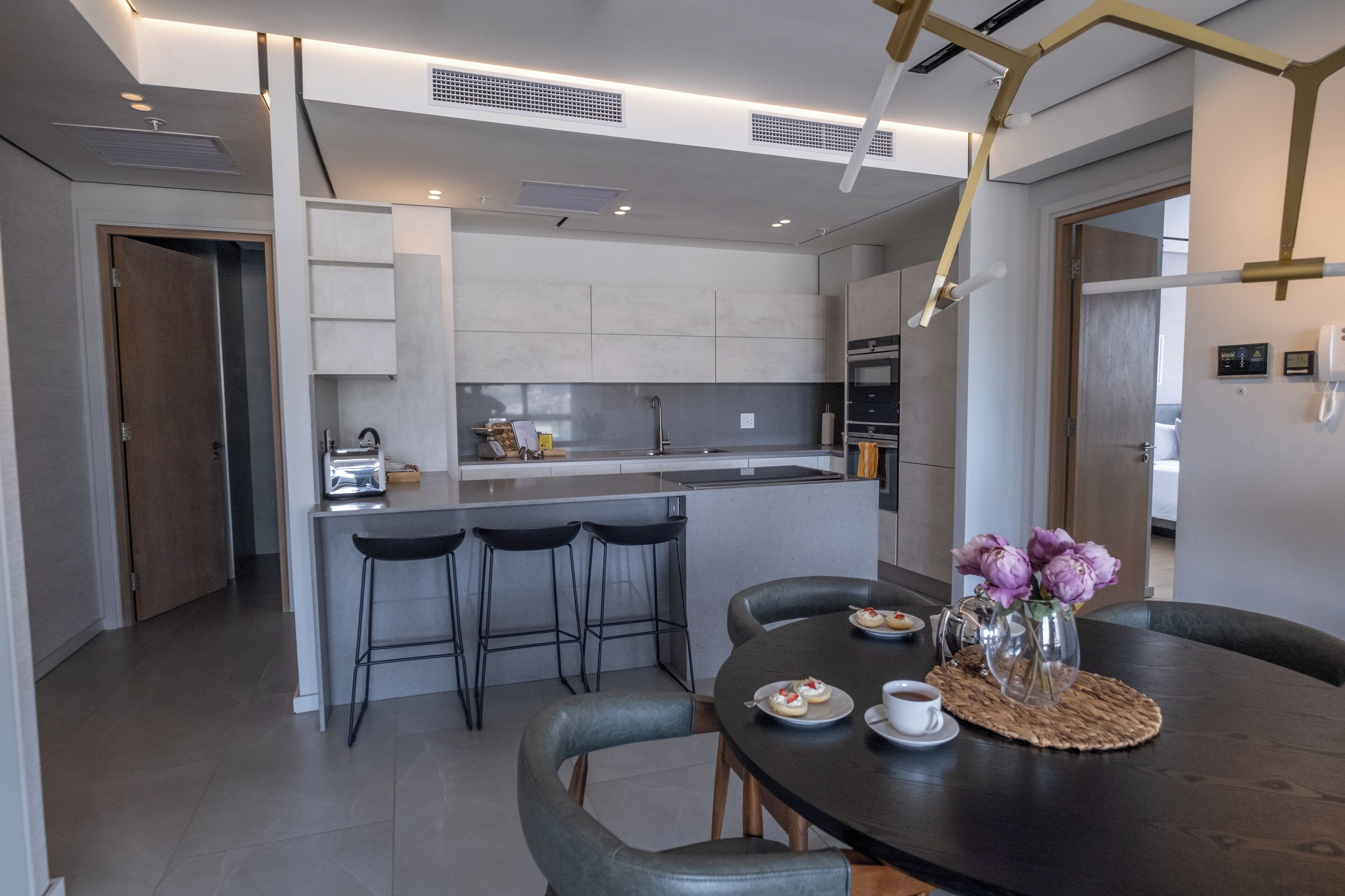 Een moderne keuken met een centraal eiland, barkrukken en een eettafel met een bloevas.