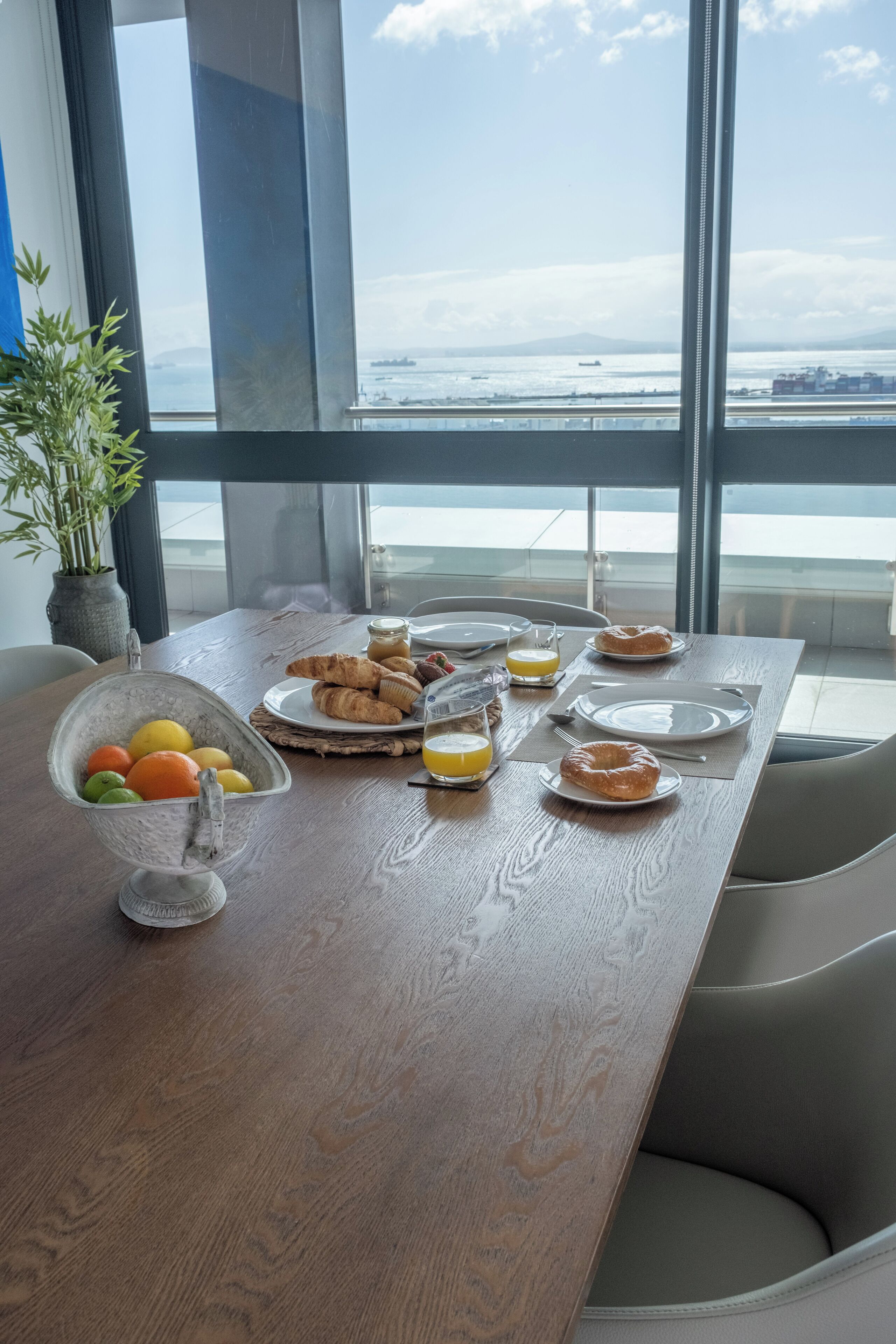 Une table de petit-déjeuner dressée avec des croissants, des pâtisseries et des fruits, le tout agrémenté d’une vue sur la mer et les montagnes.