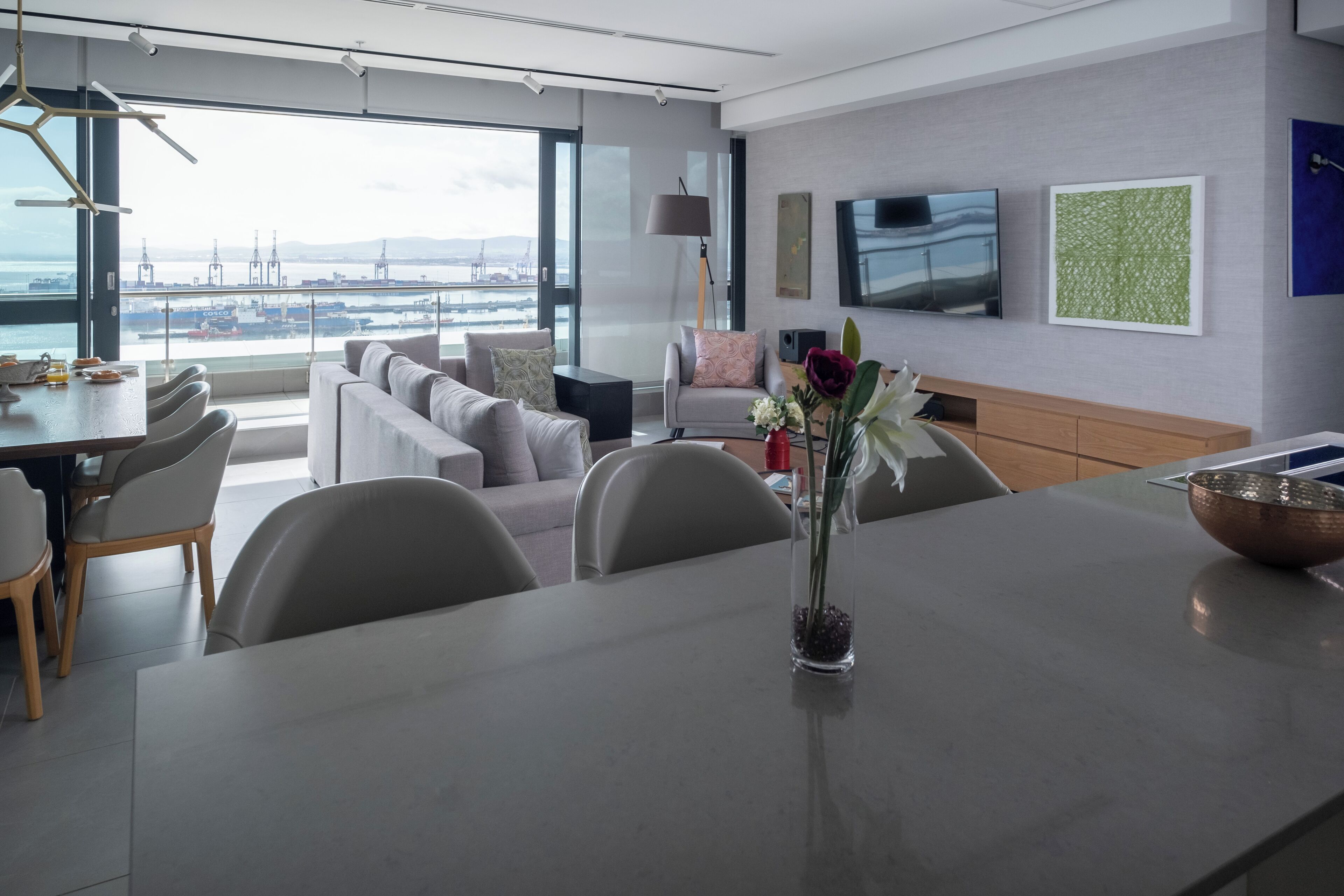 Une chambre d’hôtel moderne dotée d’un coin repas, d’un canapé, d’une télévision et offrant une vue sur le port.