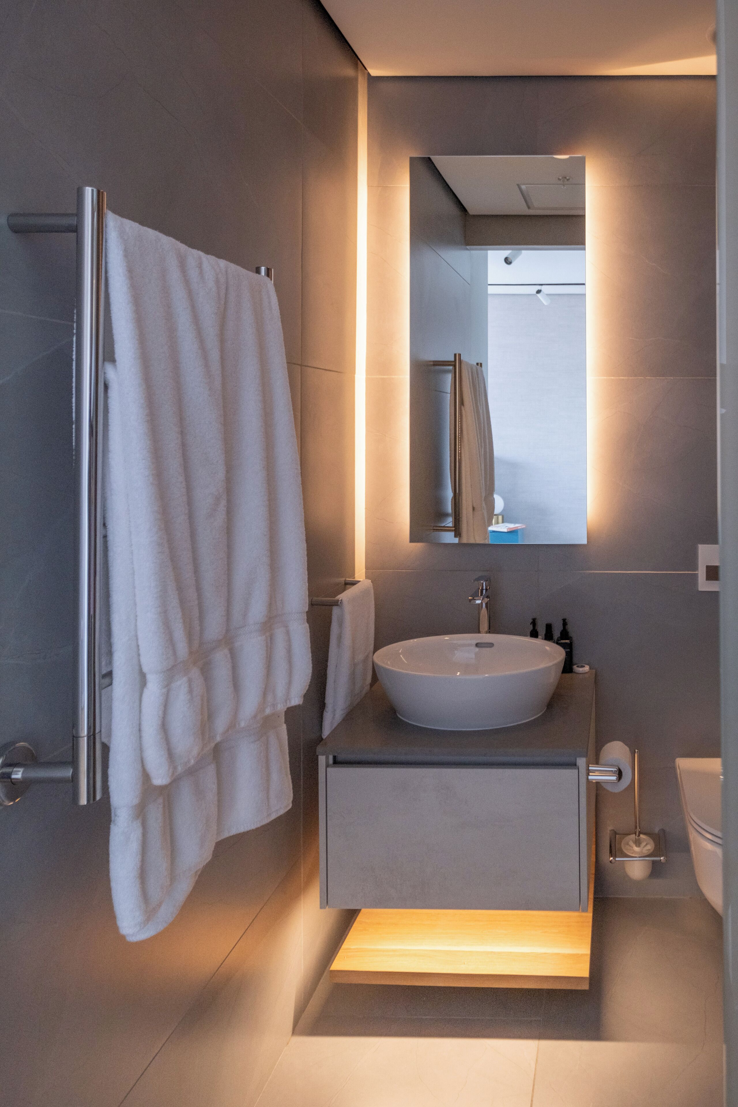 A modern bathroom with a large sink, a mirror, and a towel rack.