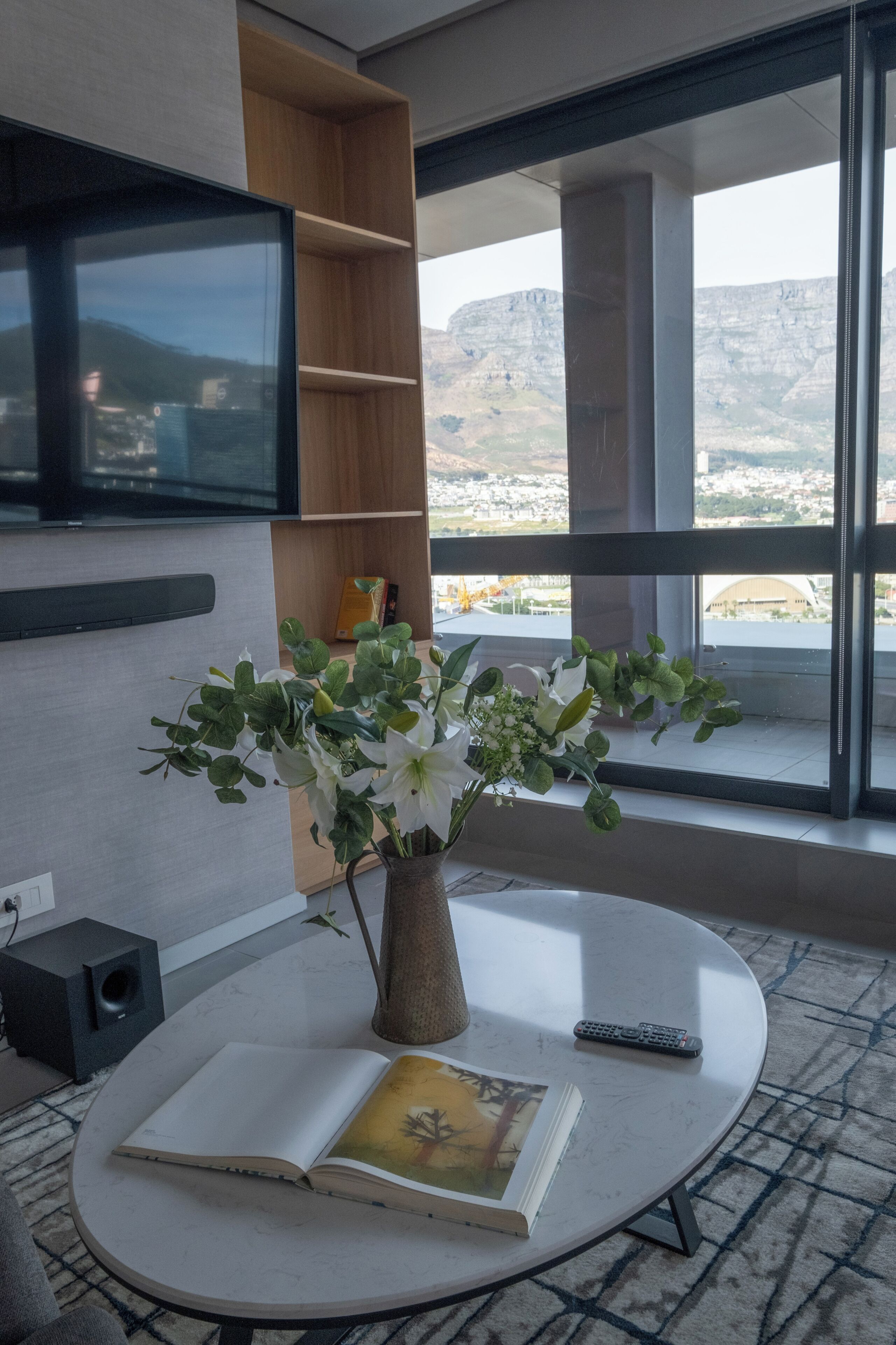Een moderne woonkamer met een ronde tafel, een boek, een afstandsbediening en een vaas met bloemen.