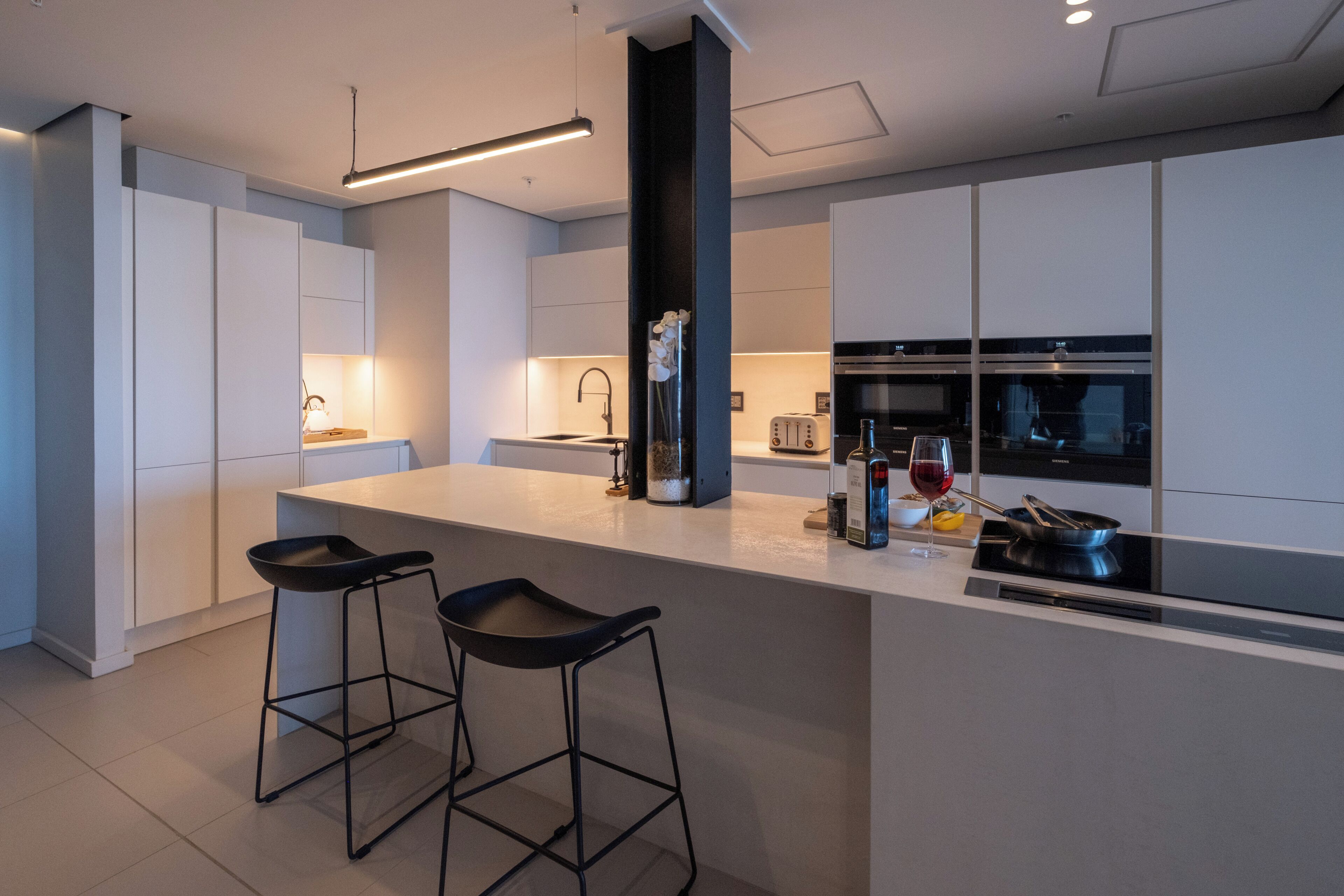 Een moderne keuken met een centraal kookeiland, barstoelen, een ingebouwde oven en een wijnglas.