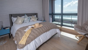 A modern bedroom with a large bed, a view of the sea, and a balcony. - The Halyard Apartments  (Cape Town)