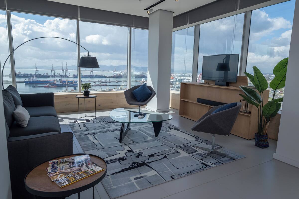 Una sala de estar moderna con un sofá, una mesa de centro de vidrio, un televisor y vistas a un puerto con barcos.