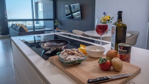 A modern kitchen with a built-in stove, a cutting board with mushrooms, a wine glass, a bottle of olive oil, and a can of tomatoes. - The Halyard Apartments  (Cape Town)