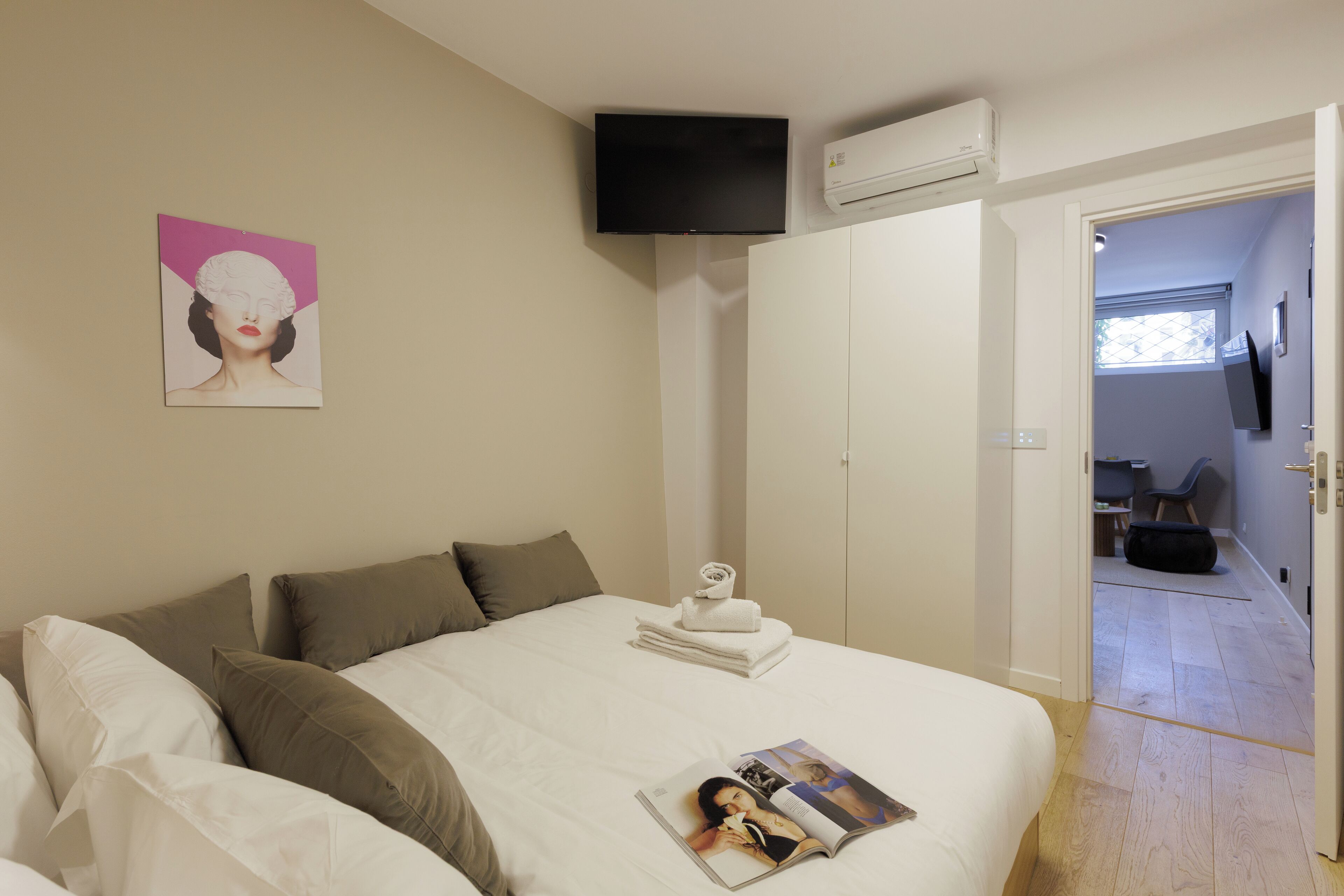 Une chambre à coucher avec un lit, des oreillers, un téléviseur à écran plat, un climatiseur et un magazine posé sur le lit.