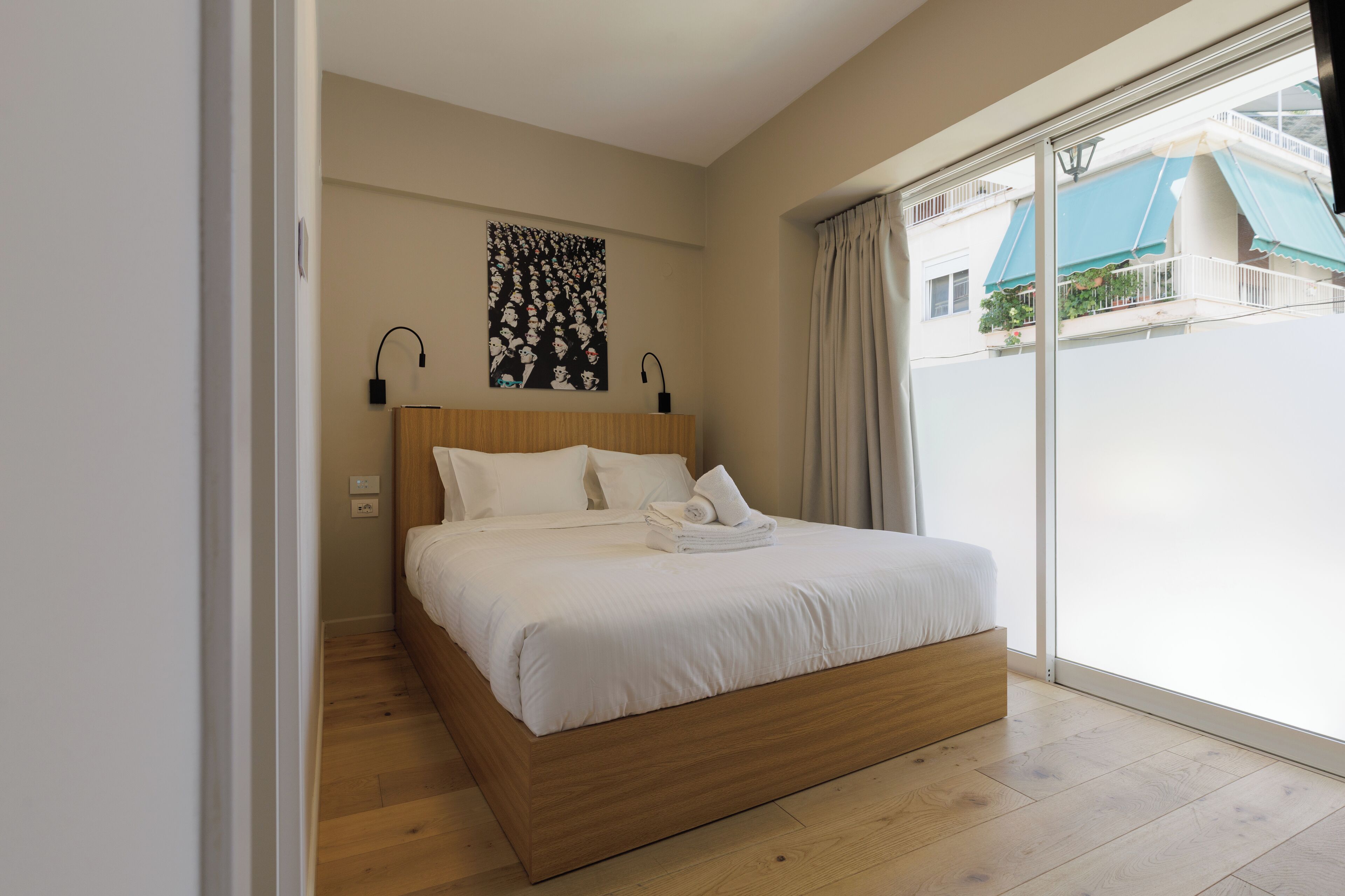 A bedroom with a wooden bed, white bedding, a wall-mounted artwork, and a view of the outside balcony.