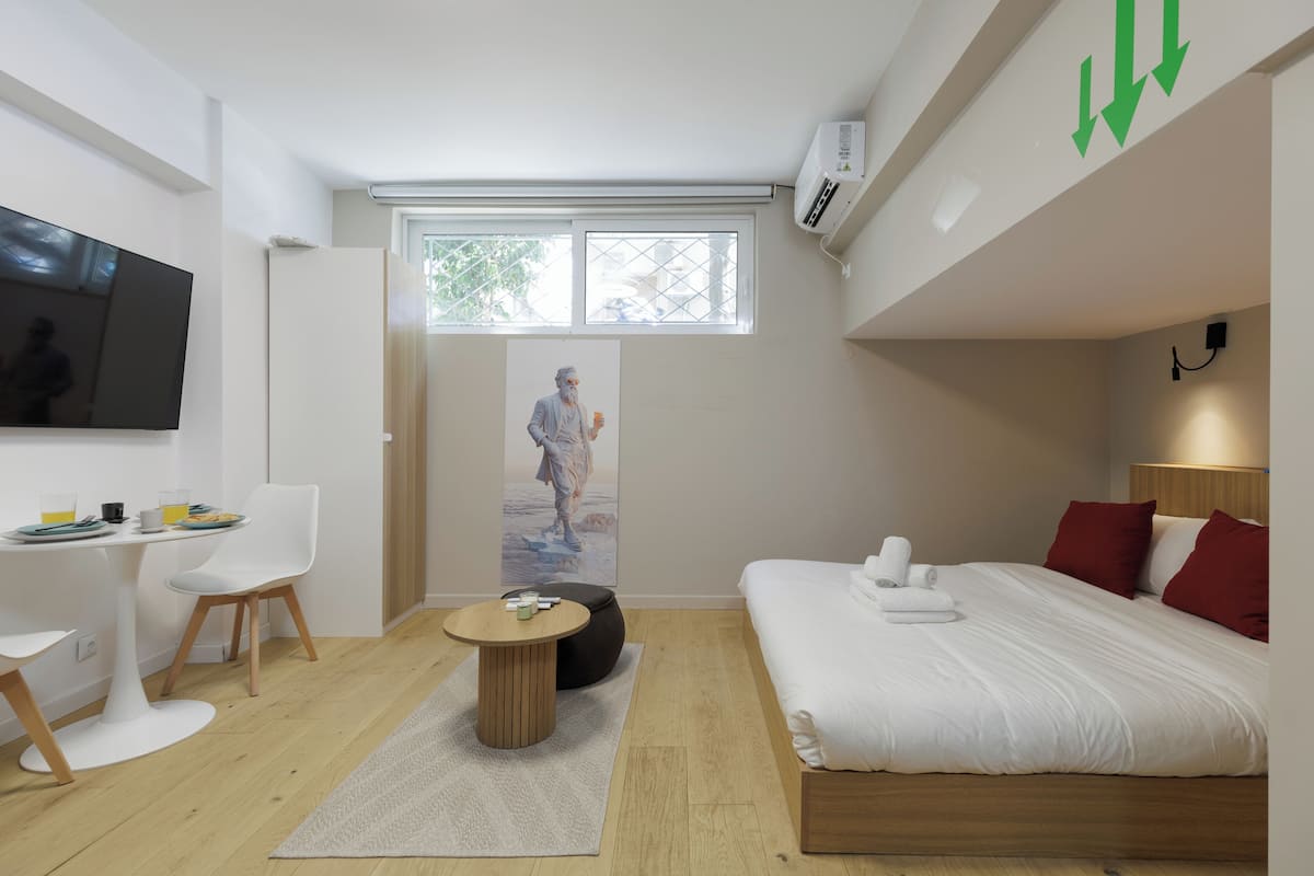 Ein modernes Hotelzimmer mit einem Bett, einem Schreibtisch, einem Sessel, einem runden Tisch und einem großen Fenster.