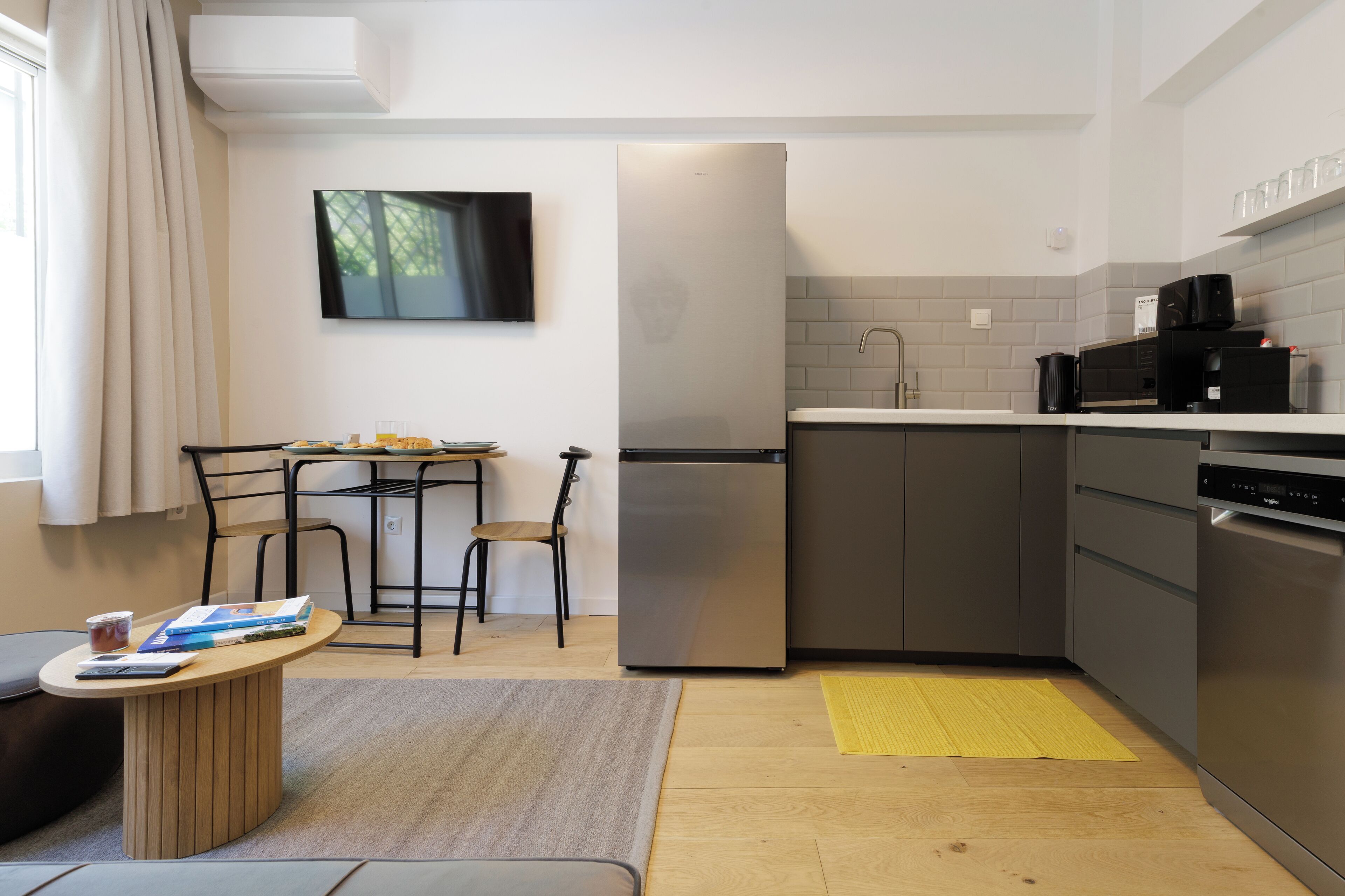 A compact kitchen with a refrigerator, microwave, and sink. There's a small dining table with chairs and a rug on the floor.