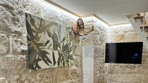 Una stanza con parete in pietra, un quadro, una TV a schermo piatto e un tavolo pieghevole con sedie.