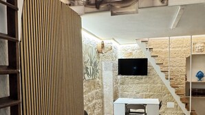 Un interno moderno con pavimento in legno, una scrivania bianca, un televisore fissato a una parete in pietra e una scala.