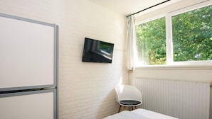 Una camera da letto con un letto, una TV a parete, una sedia e una finestra vista alberi.