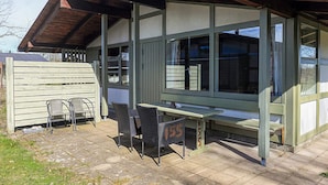 A covered patio area with a table and chairs, a wooden fence, and a building with large windows. - 6 Person Holiday Park Home in Gilleleje (Gilleleje)