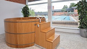 A wooden sauna with steps leading into it, a large window with a view of a swimming pool outside, and potted plants on either side. - 6 Person Holiday Park Home in Gilleleje (Gilleleje)