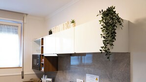 Une cuisine moderne avec des meubles blancs, un four à micro-ondes, une bouilloire et une plante suspendue.