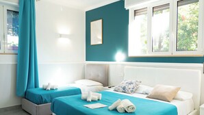 Une chambre d’hôtel avec deux lits, une literie de couleur turquoise, des têtes de lit blanches et une fenêtre avec des rideaux.