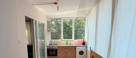 A spacious living area with a sofa, a kitchen with a washing machine, and a sliding glass door leading to a balcony.