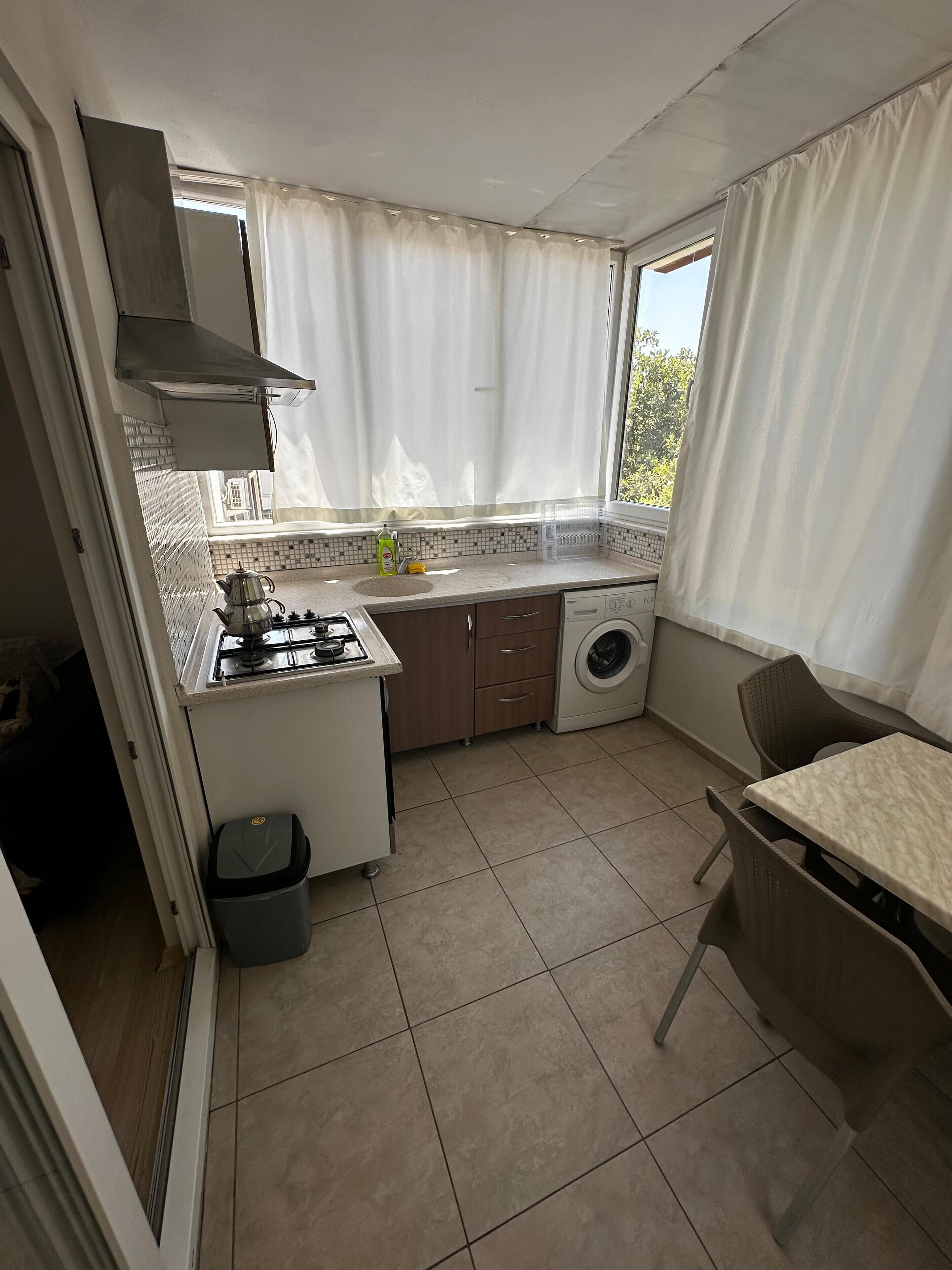 Una cocina compacta con estufa a gas, lavadora y comedor con mesa y sillas.