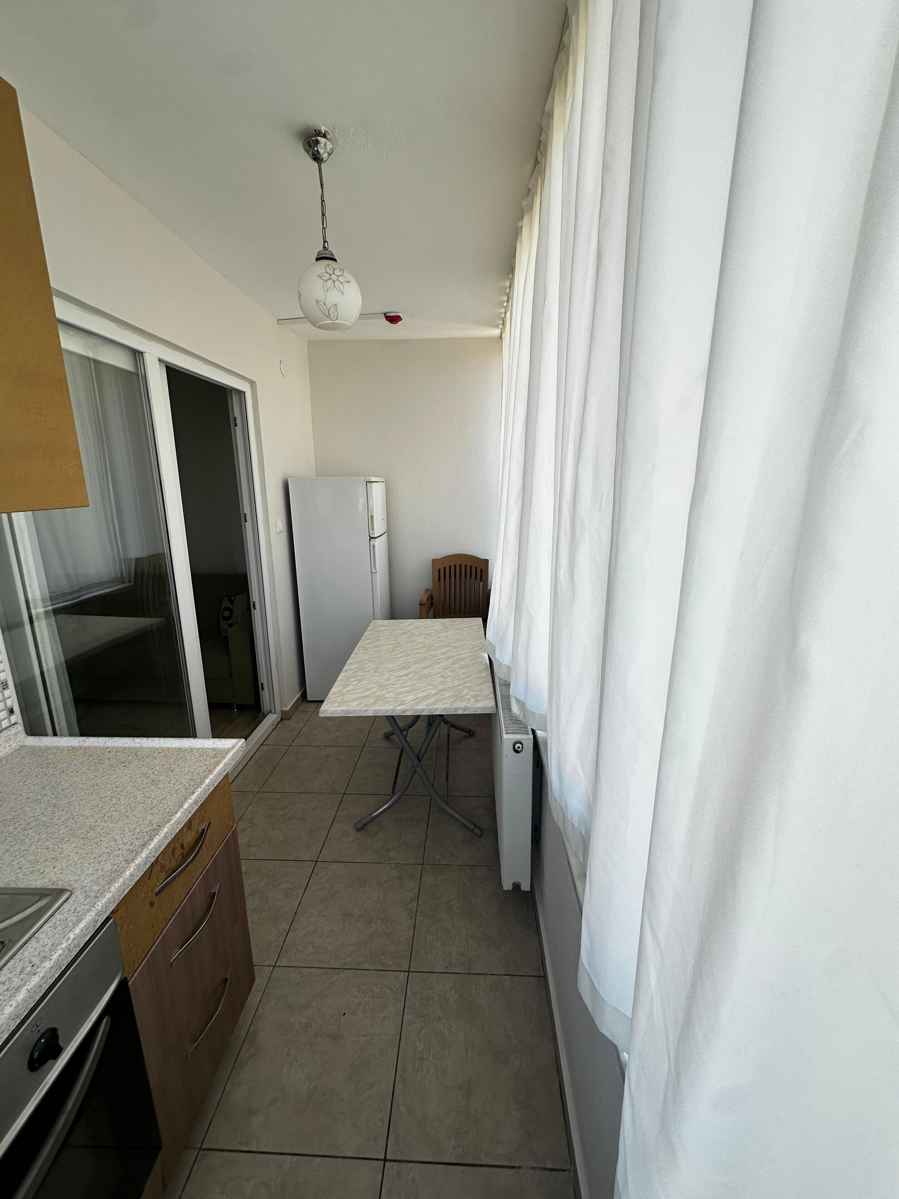 A compact kitchen with a refrigerator, a table, and a window with curtains.