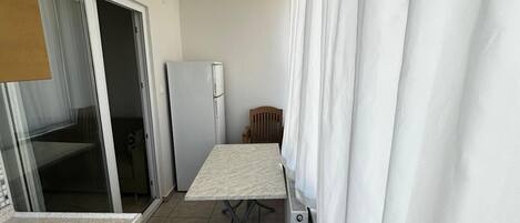 A compact kitchen with a refrigerator, a table, and a window with curtains.