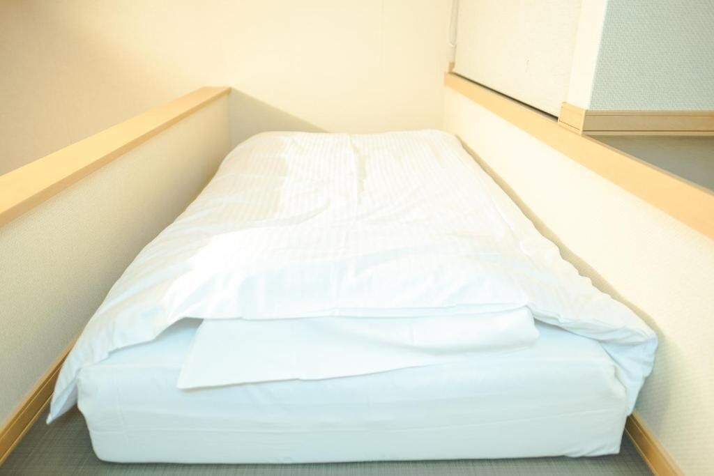 Een kleine, smalle hotelkamer met een enkel bed en een houten hoofdeinde.