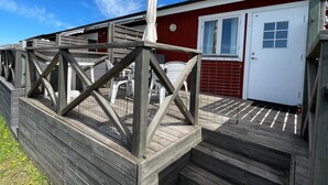 Eine Holzterrasse führt zu einem Gebäude mit einer weißen Tür und Fenstern.