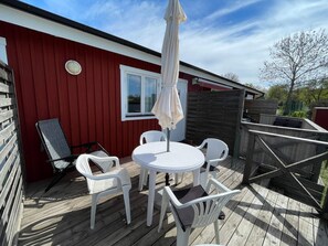 A red building with a deck, white chairs, a table, and an umbrella. - 4 Person Holiday Home in Kopingsvik (Kopingsvik)