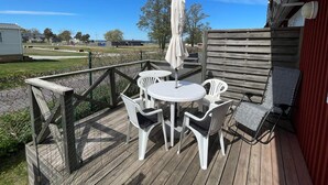 Eine Holzterrasse mit Gartenmöbeln, darunter ein Tisch und Stühle, und ein überdachter Sonnenschirm.