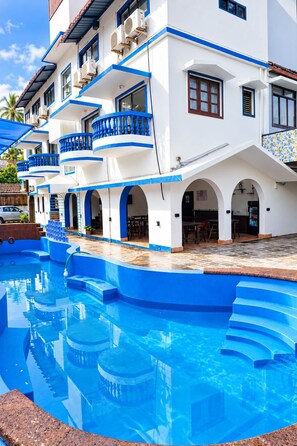 A hotel with a swimming pool, multiple balconies, and a tiled patio area. - Omnia Beach Resort Near Candolim Beach (Candolim)