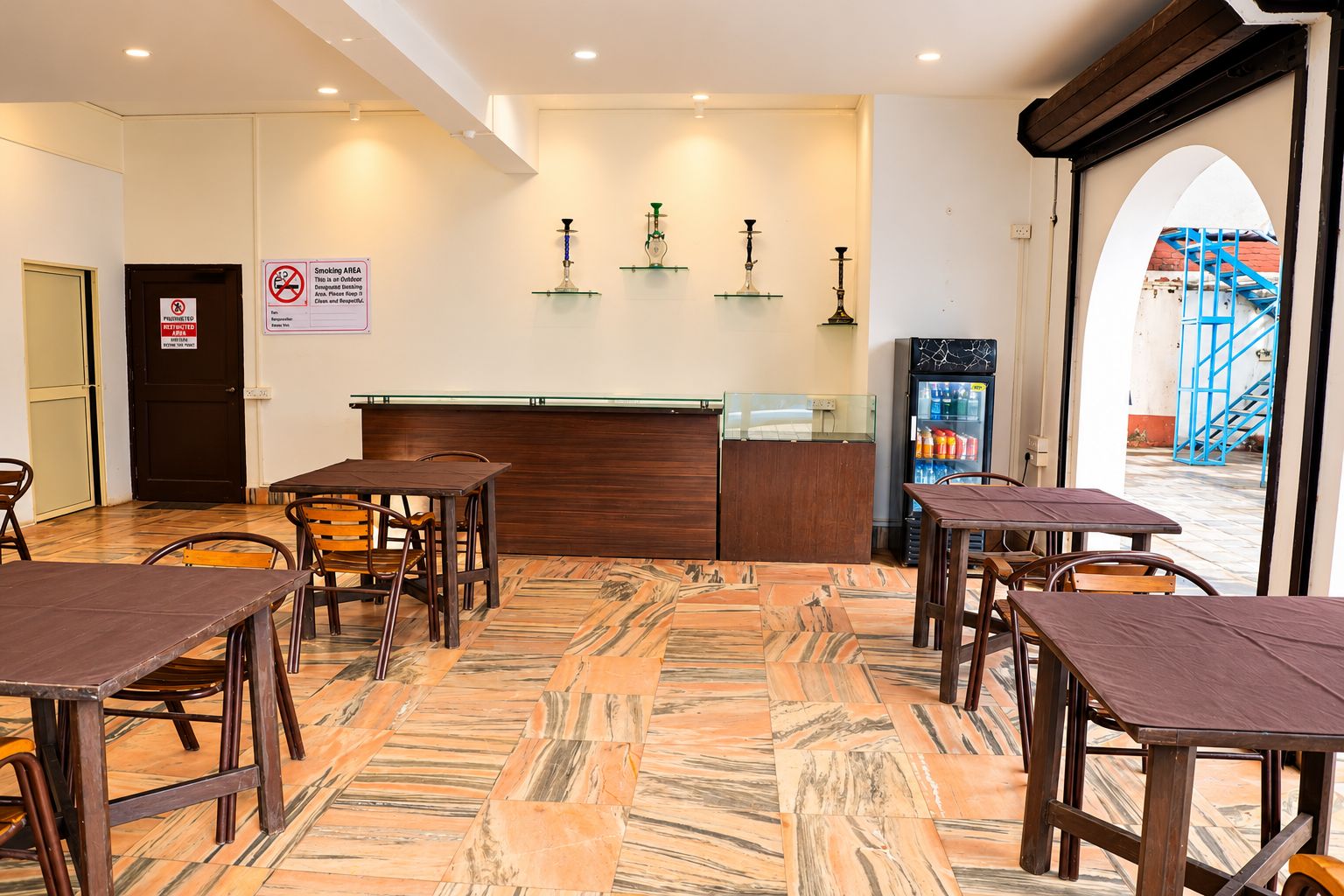 A restaurant interior with a marble floor, wooden tables and chairs, a counter with a cash register, and a sign prohibiting smoking outdoors.