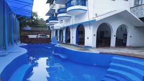 Une piscine avec des marches bleues menant à l’eau, entourée d’un bâtiment aux murs blancs et aux touches de couleur bleue.
