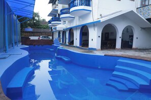 Una piscina con gradini azzurri che conducono all'interno, circondata da un edificio con pareti bianche e dettagli blu.