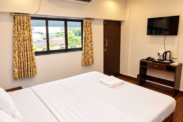 A hotel room with a large bed, a desk with a flat-screen TV, and a window with curtains. - Omnia Beach Resort Near Candolim Beach (Candolim)