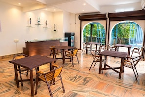 Restaurante com mesas e cadeiras de madeira, balcão de recepção e vista através de amplas janelas em arco.