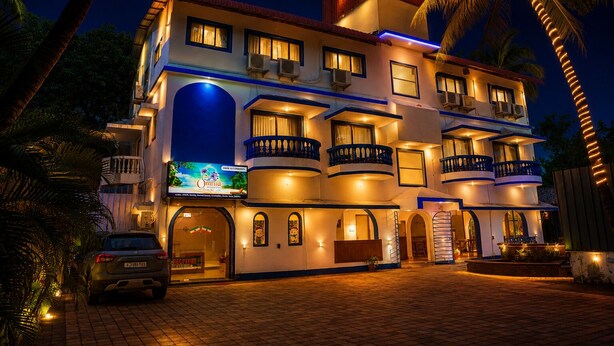 A multi-story hotel with balconies, a reception area, and a car parked in front. - Omnia Beach Resort Near Candolim Beach (Candolim)