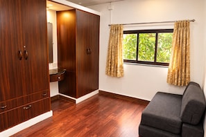 A room with a wooden wardrobe, a small sink, a window with curtains, and a grey sofa. - Omnia Beach Resort Near Candolim Beach (Candolim)