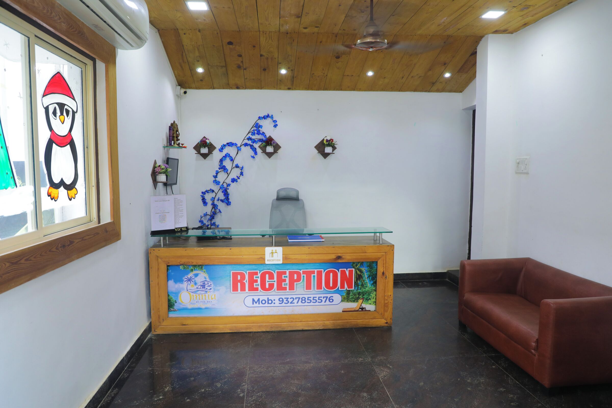 Zona de recepción con techo de madera, mostrador de recepción, sofá y un letrero en la pared.