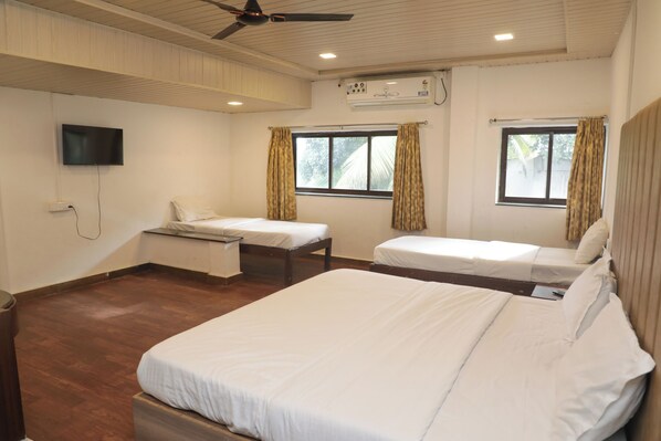 Habitación de hotel con dos camas individuales, ventilador de techo, unidad de aire acondicionado, televisor montado en la pared y ventana con cortinas.