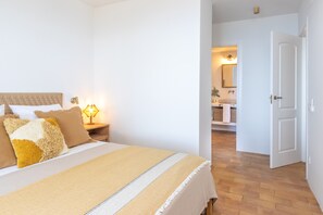 A bedroom with a bed, bedside table, lamp, and an open door leading to a bathroom.