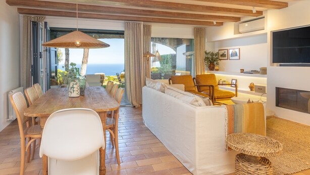 Un amplio salón con una mesa de comedor de madera, sofá blanco y vistas al mar.