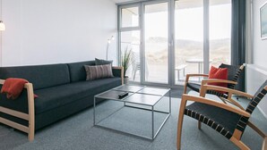 Ein modernes Wohnzimmer mit einem dunkelgrauen Sofa, einem Glastisch und zwei Holzstühlen mit schwarzen und roten Kissen.