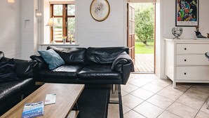 Una habitación con un sofá de cuero negro, una mesa de madera, un tocador blanco y una ventana con vistas a la vegetación.