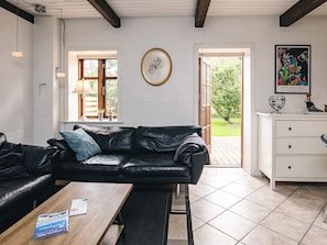 Ein Zimmer mit einer schwarzen Ledersofa, einem Holztisch, einer weißen Kommode und einem Fenster mit Blick auf Grünflächen.